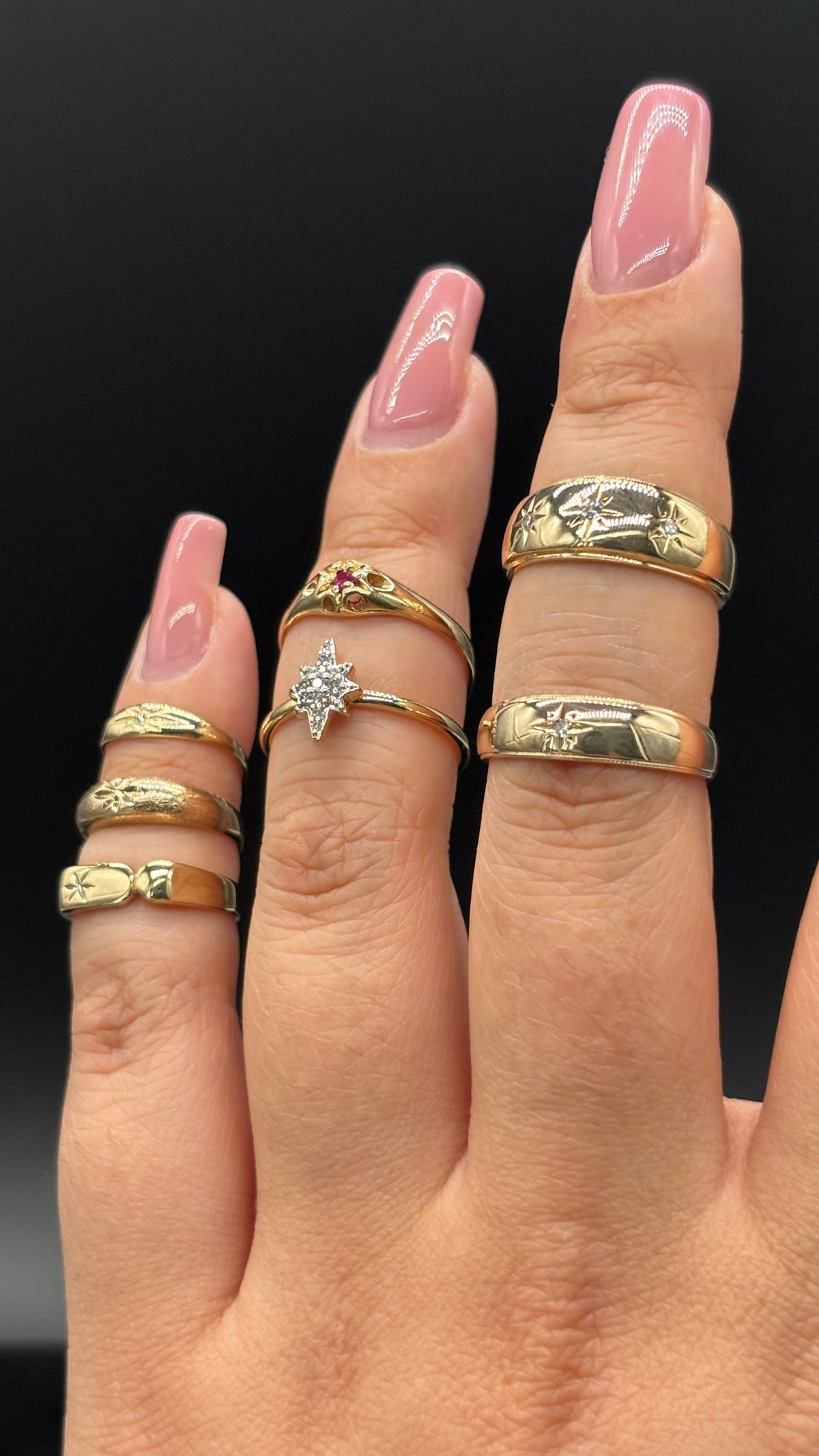 Stacked vintage gold rings on hand including engraved bands and a star-set diamond ring