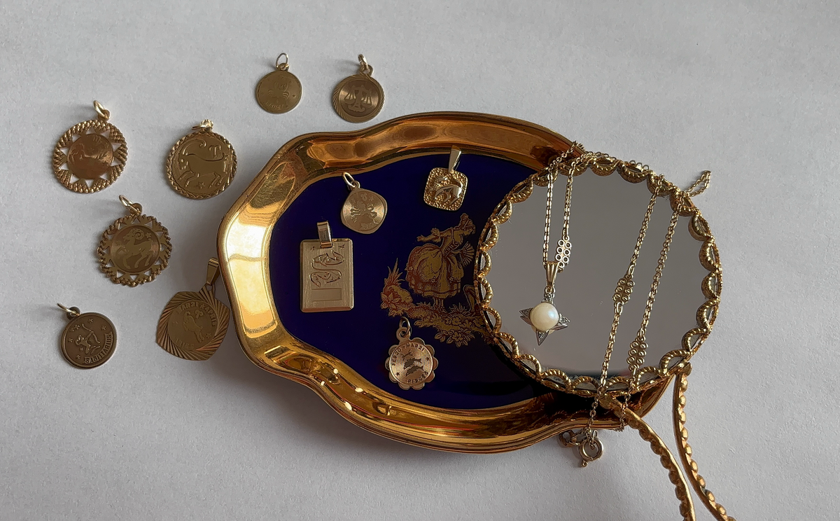 Vintage gold charm collection featuring zodiac medallions and a pearl star pendant displayed on a blue enamel tray with gold trim
