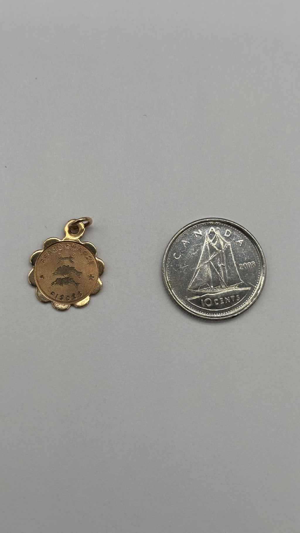 10k solid gold Pisces charm with scalloped edge next to Canadian 10 cent coin for size reference
