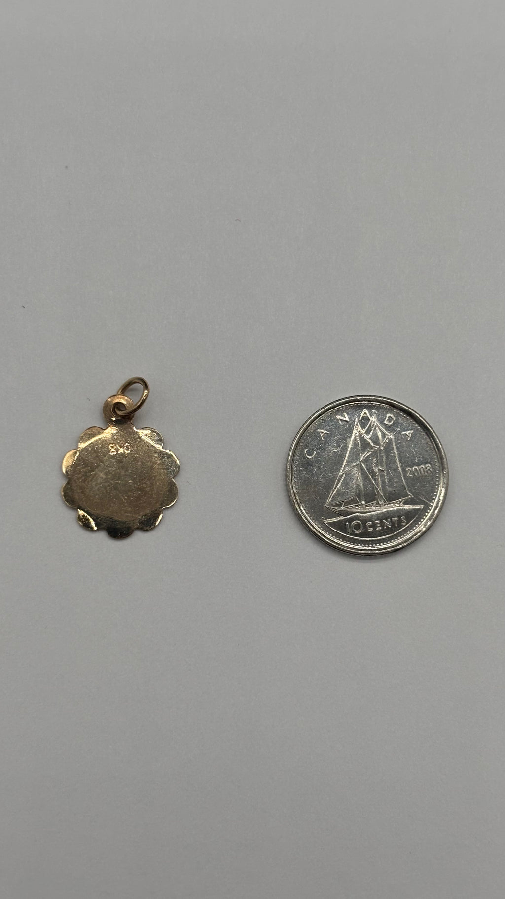 Back of 10k solid gold Pisces charm with scalloped edge next to Canadian 10 cent coin