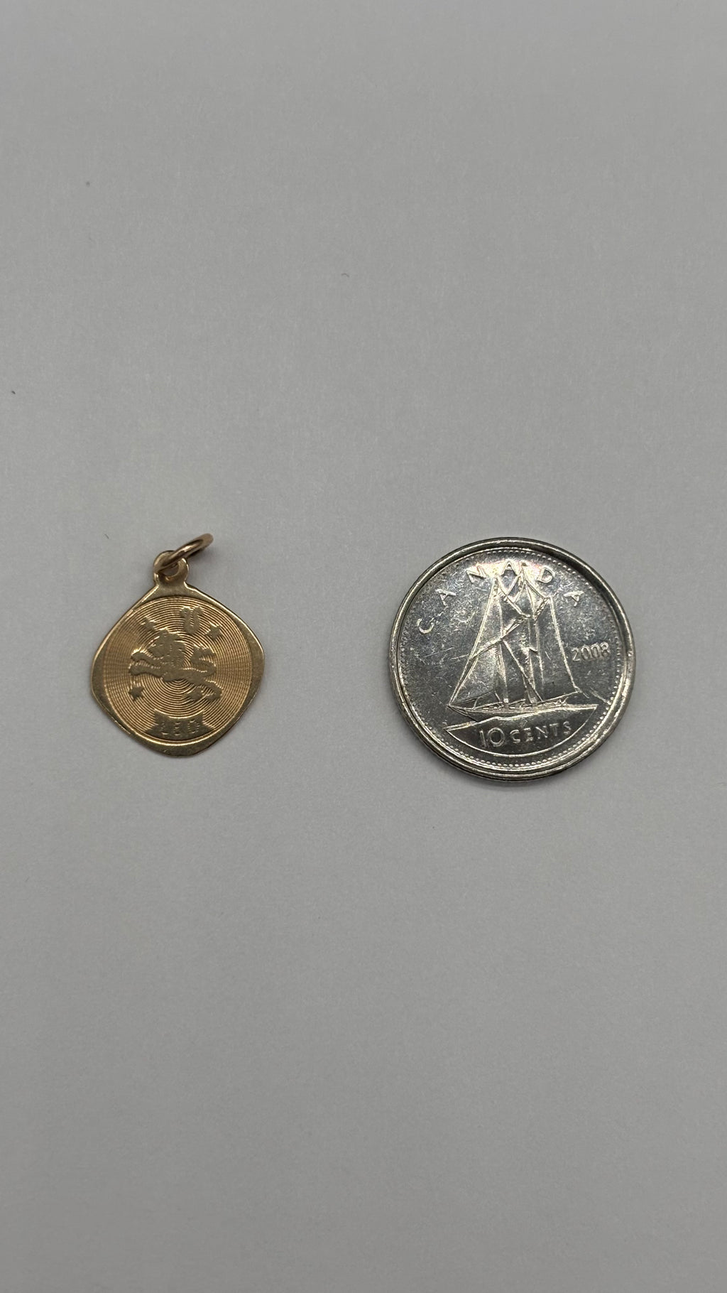 10k solid gold Leo charm next to Canadian 10 cent coin for size reference
