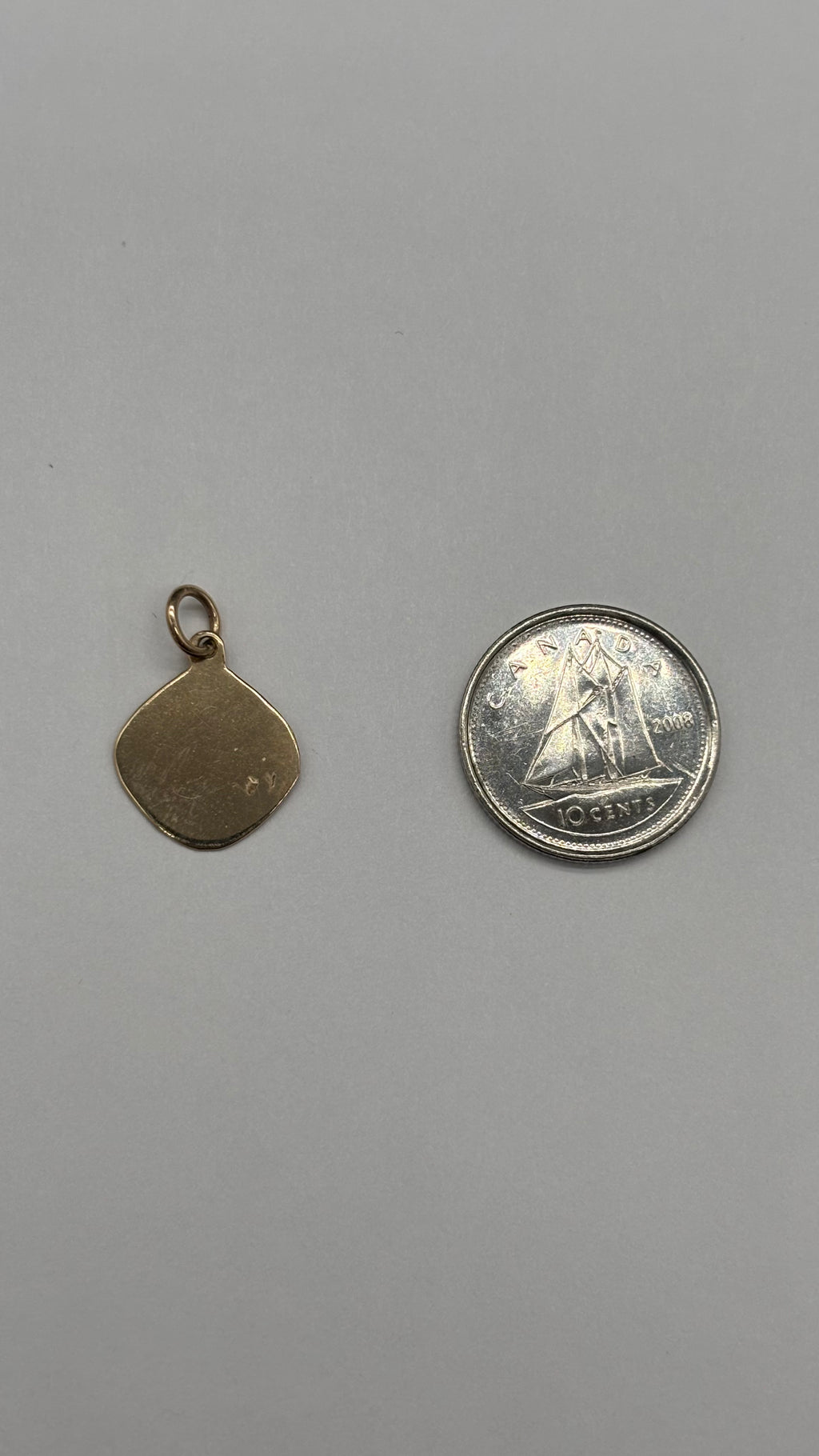 Back of 10k solid gold Leo charm next to Canadian 10 cent coin