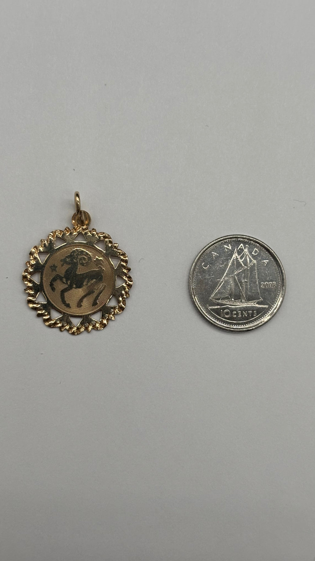 10k solid gold Aries charm with diamond cut scalloped edge next to Canadian 10 cent coin for size reference