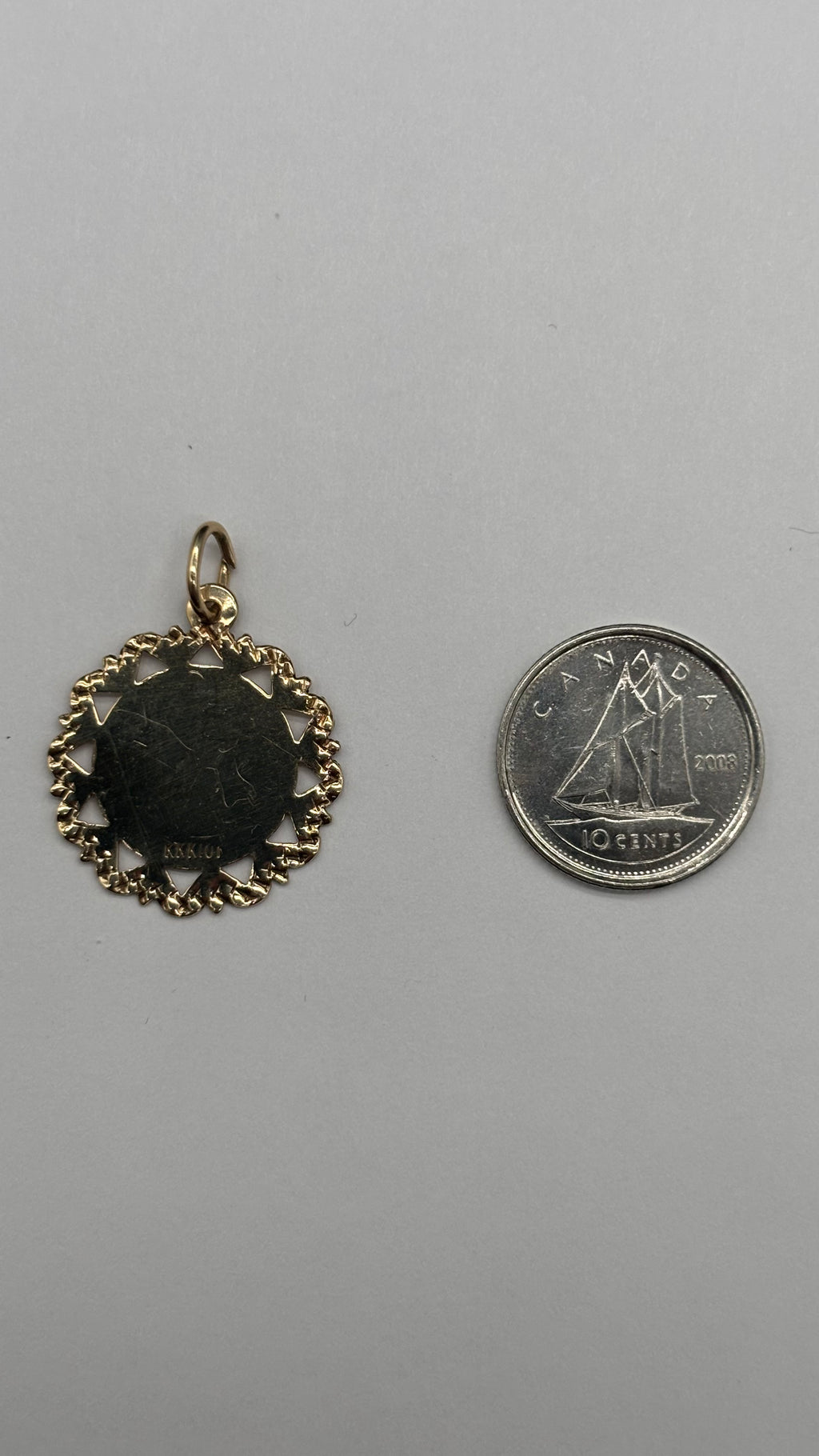 Back of 10k solid gold Aries charm with diamond cut scalloped edge next to Canadian 10 cent coin