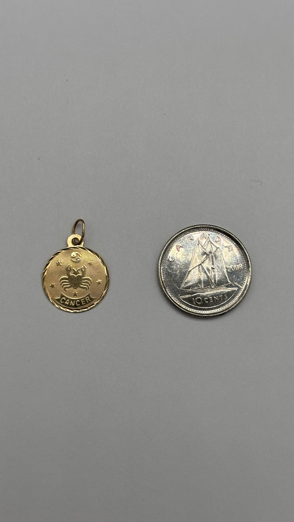 14k solid gold circular Cancer charm next to Canadian 10 cent coin for size reference