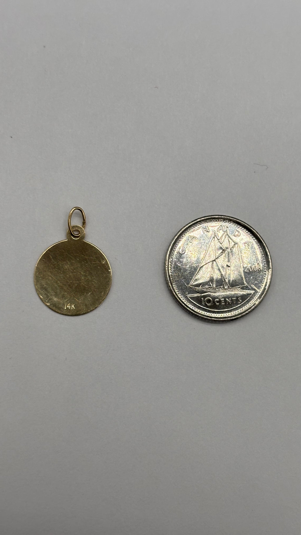 Back of 14k solid gold circular Cancer charm next to Canadian 10 cent coin