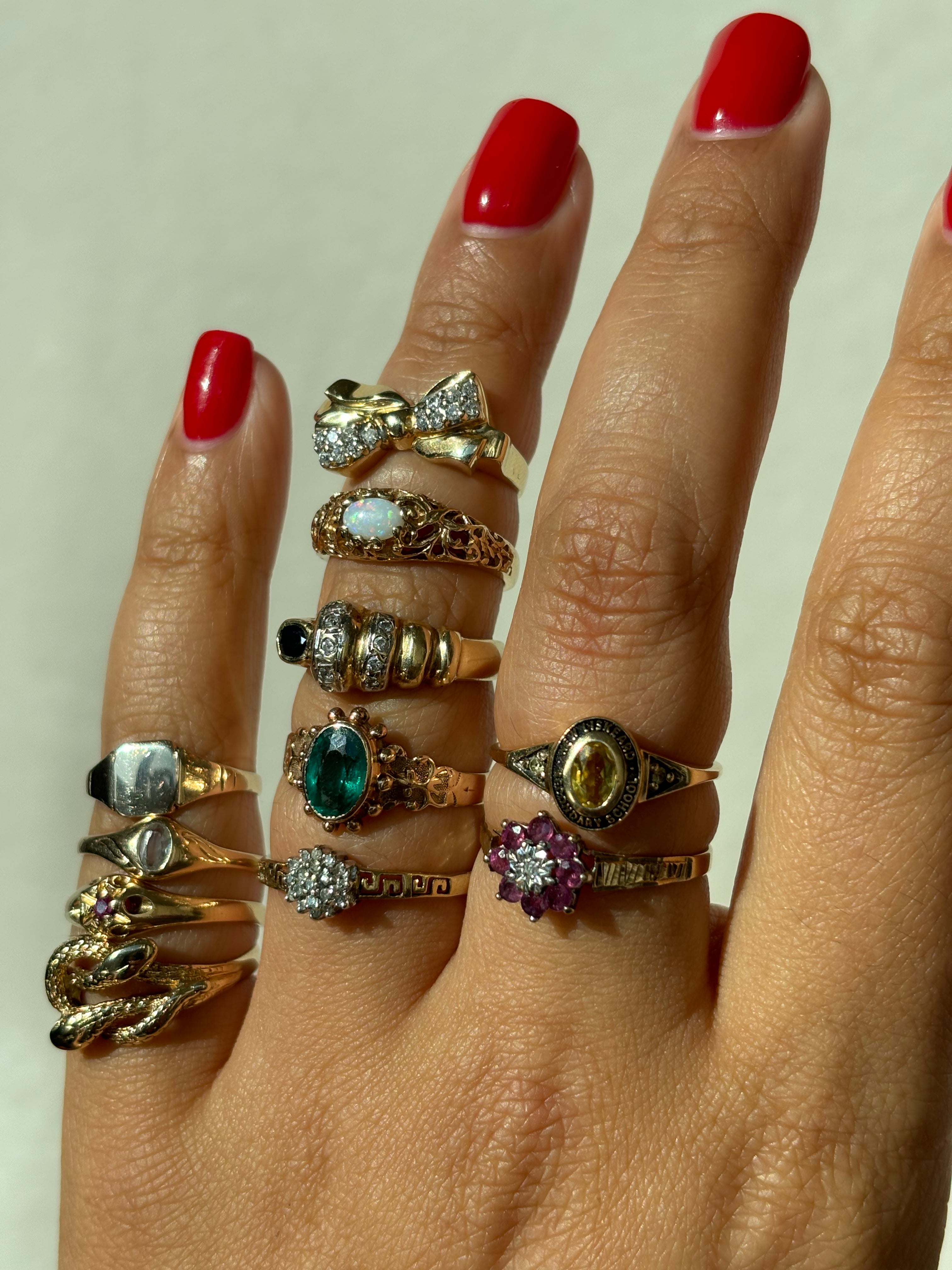 Stacked vintage gold rings on hand featuring gemstone accents including opal, emerald, ruby, and diamond designs with red manicured nails