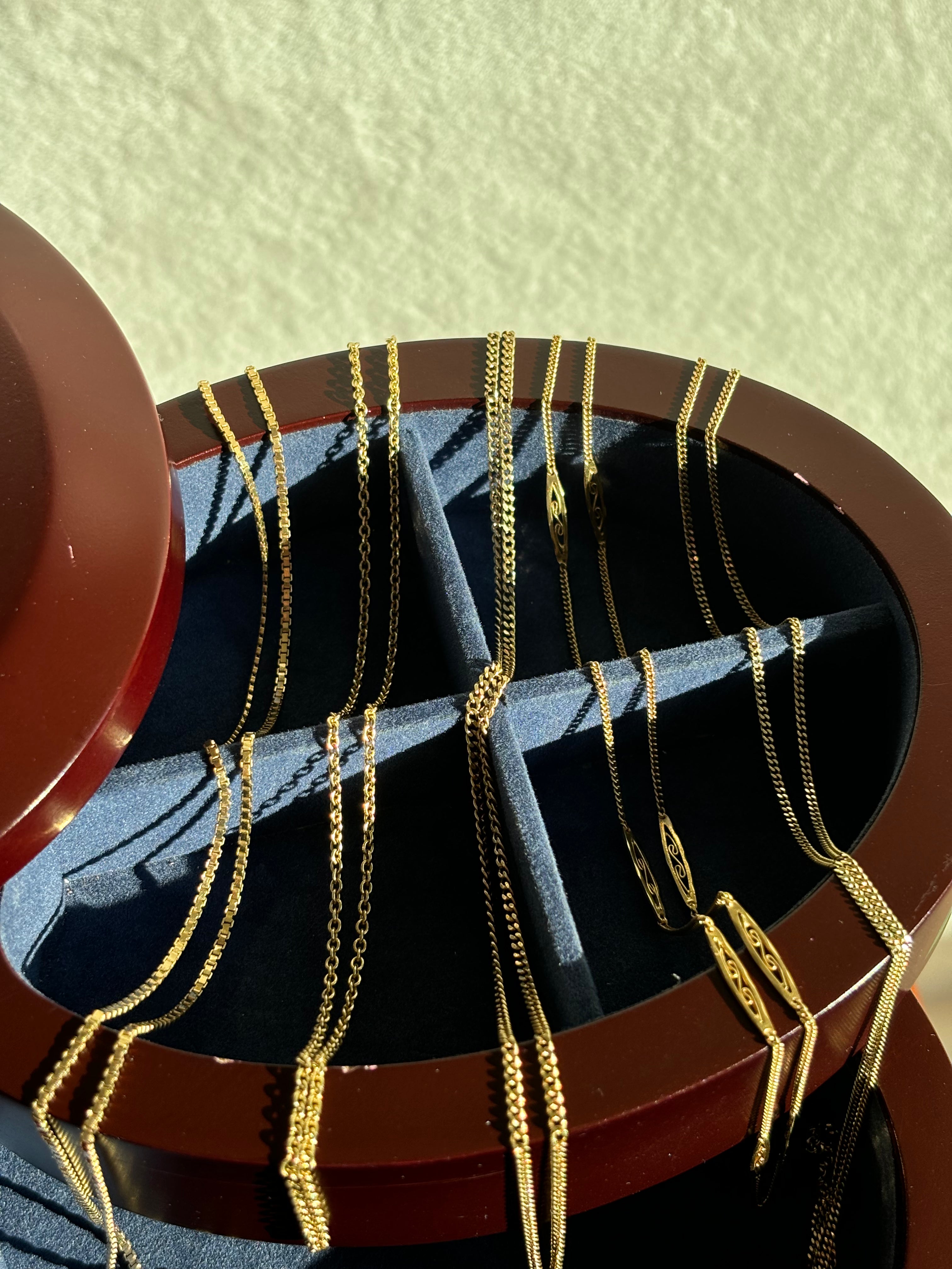 Vintage gold chain collection displayed in a round wooden velvet jewelry case featuring a variety of link styles in warm sunlight

