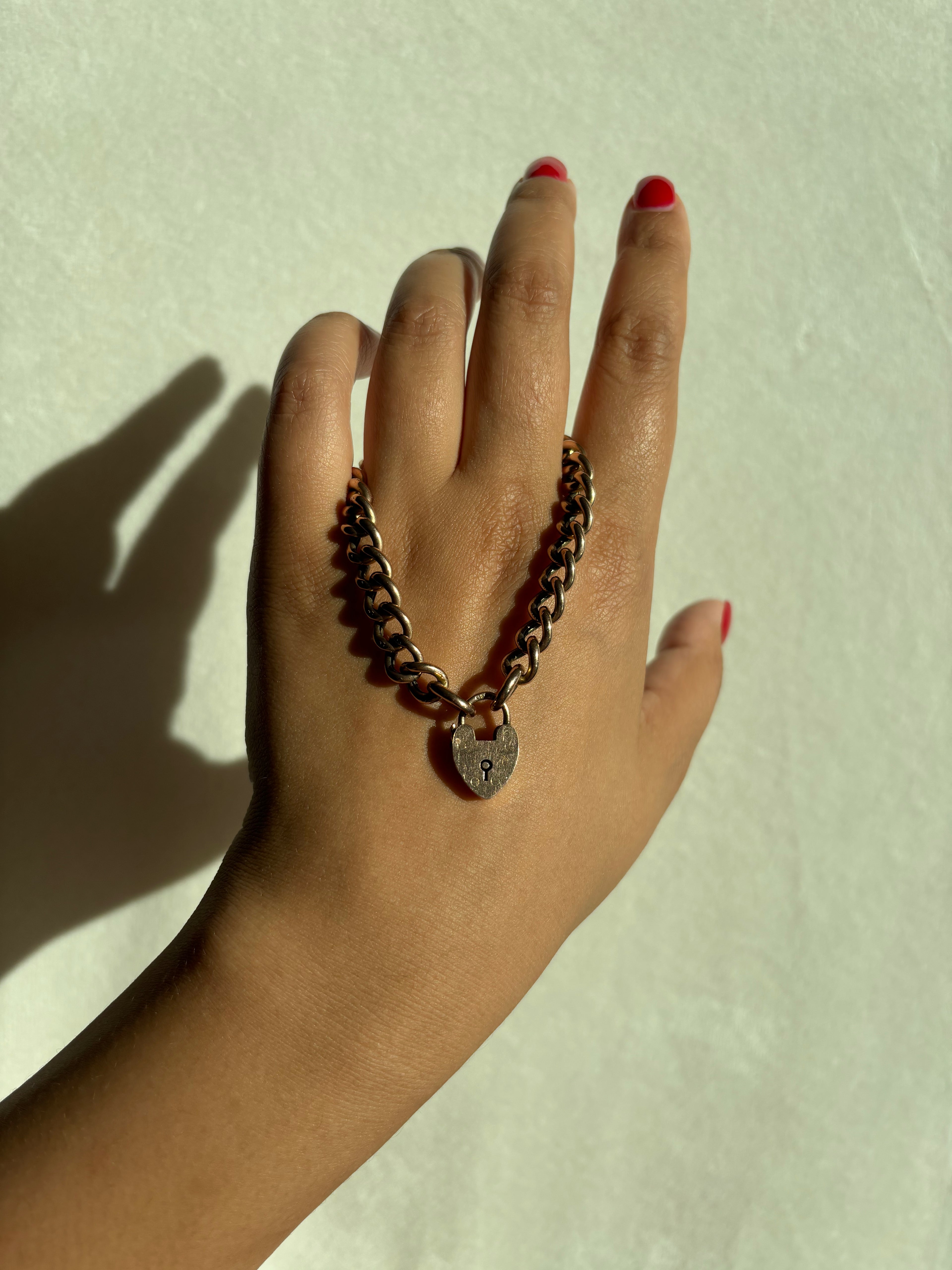 rosy gold english puffy curb heart padlock bracelet held in hand with red manicure