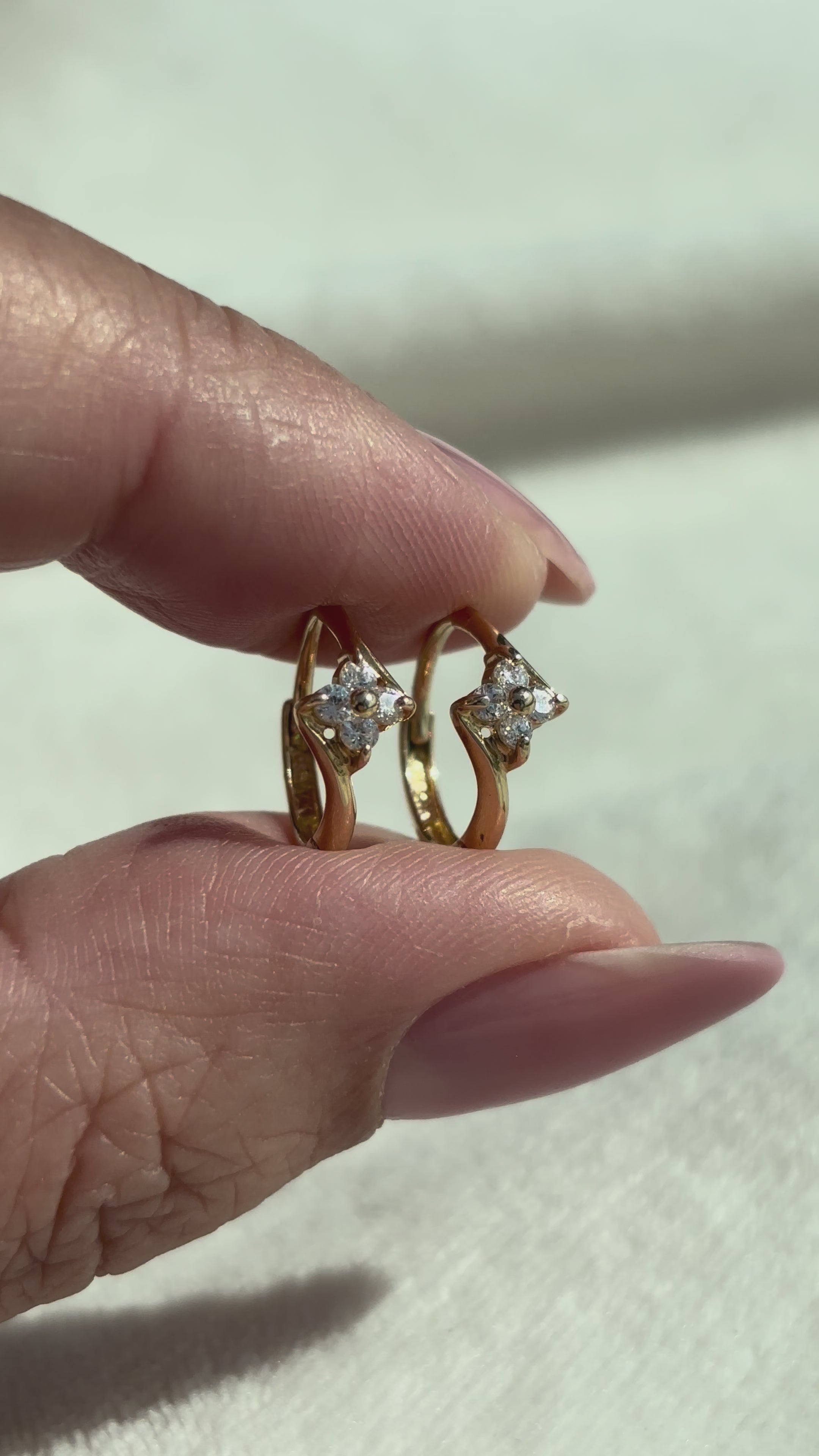 close up video of 14k Solid Gold Clear Stone Flower Huggie Hoops showing condition, shine, and stone sparkle